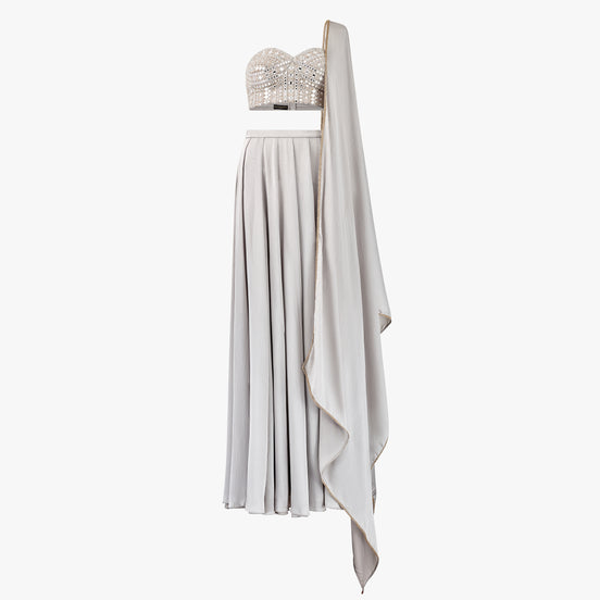 The Carlia lehenga set features a delicate mirror and chikan kari embellished bandeau top, Paired with a luxurious satin lehenga and matching dupatta, designed by Shenena Sethi